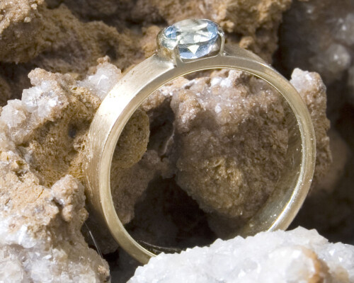 Gouden ring met aquamarijn: gematteerd goud, lichtblauwe aquamarijn in een bijzondere, halfopen zetting, geschuurd geel goud, handgemaakt door LYAM edelsmeden